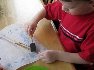 child painting wooden dowel with brown paint