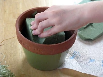 hand placing floral foam into flower pot