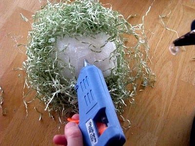 hand hot gluing craft grass onto styrofoam ball