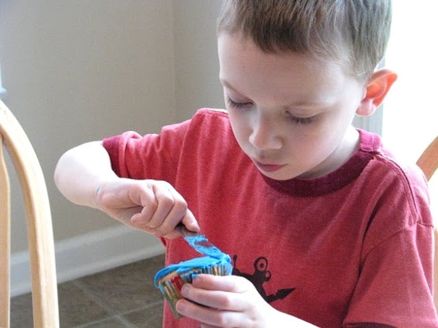 child frosting cupcake with blue frosting