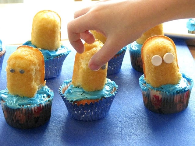 child adding Smarties candies to cupcake for eyes