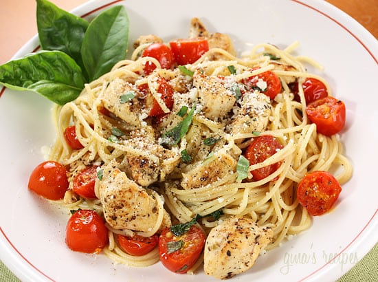 white plate with spaghetti chicken tomatoes and basil