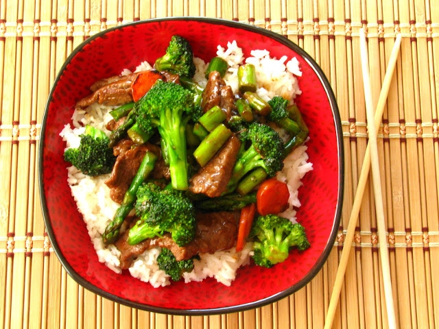 red plate with stir fry and chopsticks on bamboo placemat