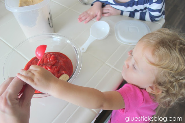 toddler hand pouring in a teaspoon of garlic powder