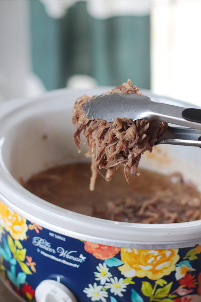tongs puling out serving of pork from slow cooker