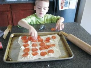 child placing pepperoni on pizza dough