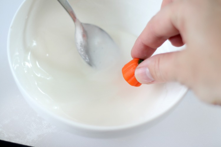 candy pumpkin being dipping into bowl of white icing