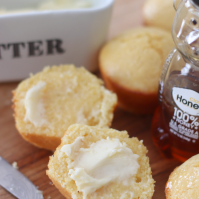 cornbread muffin sliced with butter and bottle of honey next to it