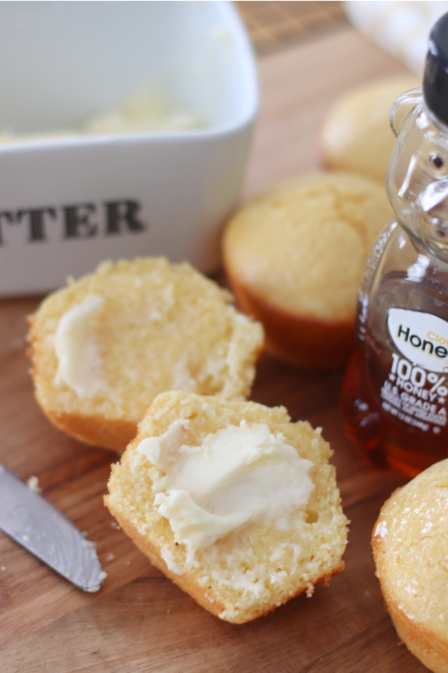 cornbread muffin sliced with butter and bottle of honey next to it