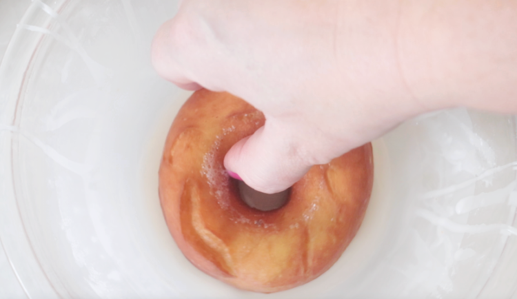hand dipping donut in glaze