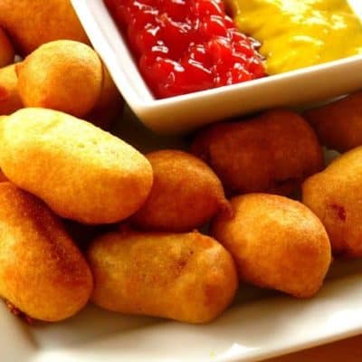 mini corn dogs on plate with bowl of condiments