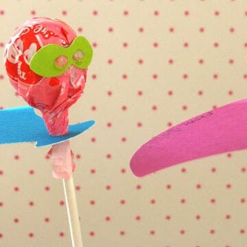 two lollipops with paper capes and masks