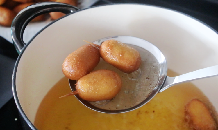 strainer over a pot of oil with fresh fried corn dog bites