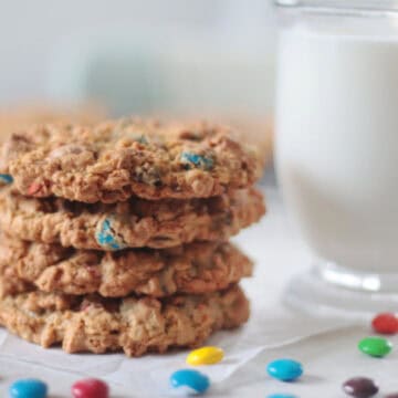 4 monster cookies stacked next to a glass of milk