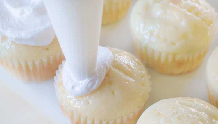 baked white cupcakes piped with whipped topping