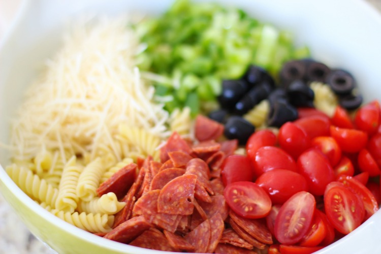 cooked pasta, pepperoni, diced tomatoes, olives, peppers and cheese in a large bowl