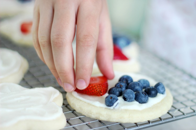 child adding fruit to mini fruit pizza