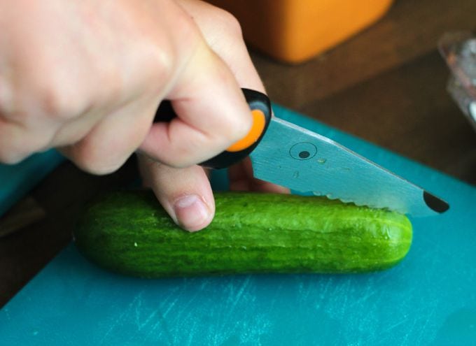 knife slicing cucumber on cutting board