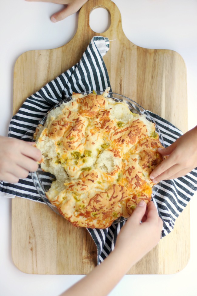 loaf of bread on bread board, hands pulling off sections to eat