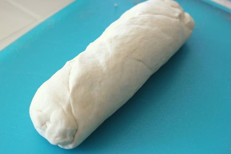 Bread dough rolled up into a loaf shape on blue cutting board.