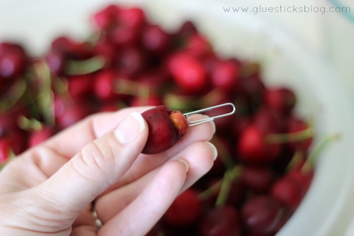 hand pitting a cherry with a paper clip