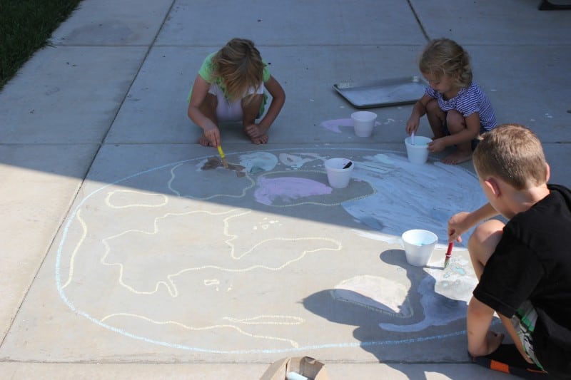 kids chalk painting a continent on the ground