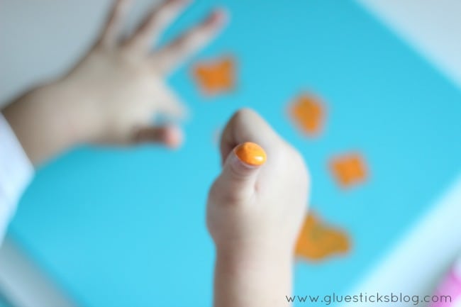 little girl with thumb dipped in orange paint