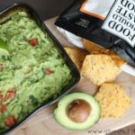 bowl of guacamole and avocado cut in half on cutting board