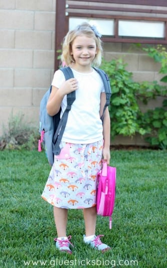 little girl wearing a backpack and holding a lunchbos