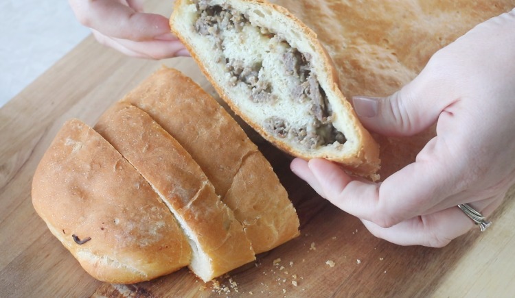 hands picking up slice of sausage bread