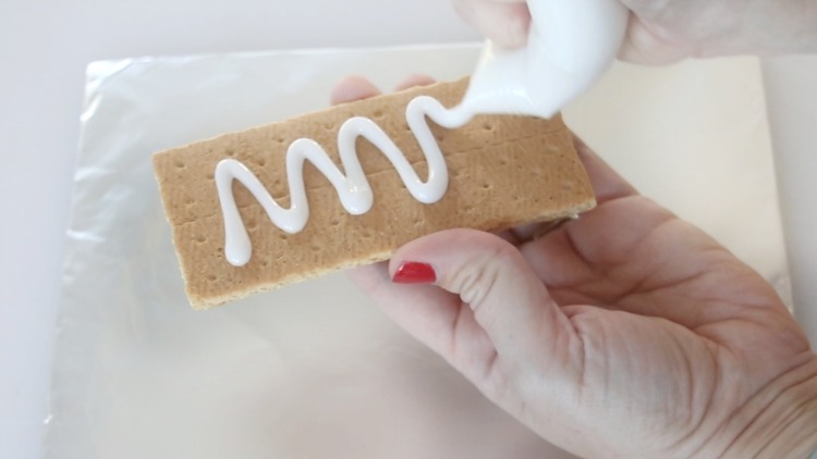 hand with piping bag adding icing to graham cracker