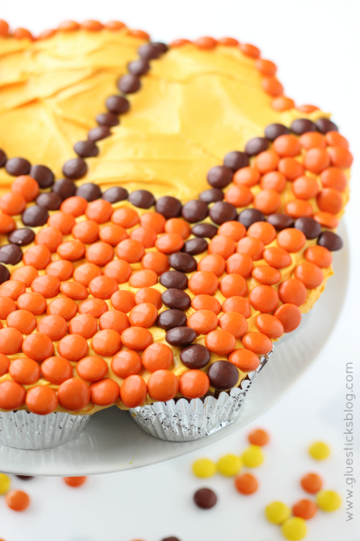 cupcakes frosted and being covered with orange and brown candies to look like basketball