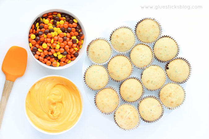 unfrosted cupcakes with bowl of frosting and bowl of candy