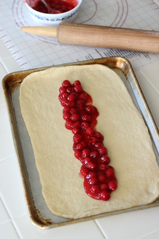 dough on baking sheet with cherry pie filling spooned down the center