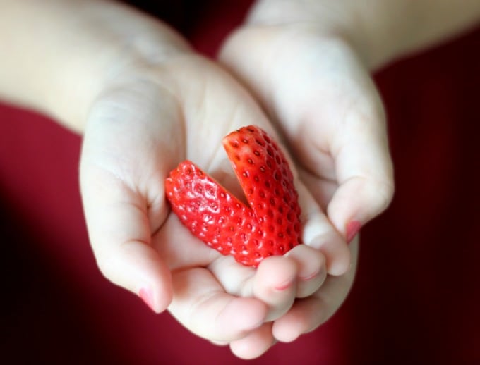 hands holding a heart shaped strawberry