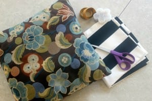 floral throw pillow next to striped fabric and scissors