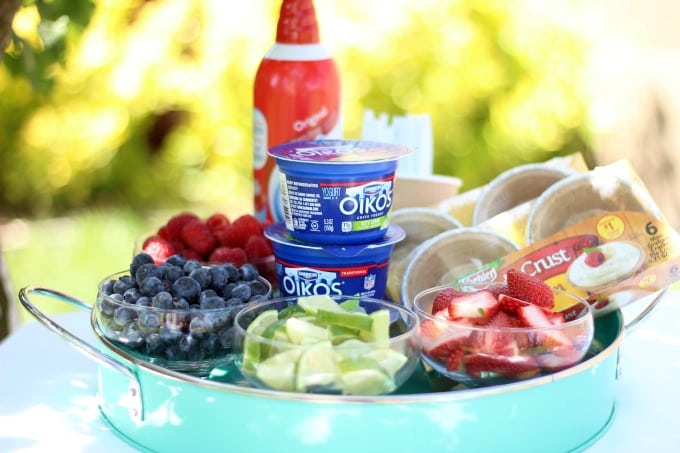 small bowls of chopped fruit, can of whipped cream, containers of lime yogurt and mini pie crusts in a serving platter