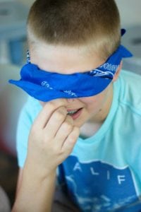 child with blindfold and plugged nose eating candy