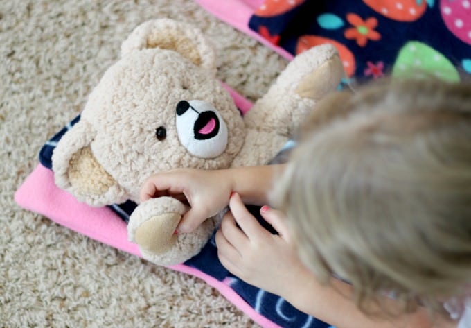 child putting teddy bear in sleeping bag