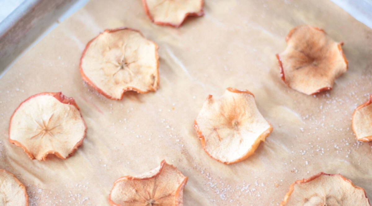 Baked apple chips on bakng sheet lined with parchment paper.