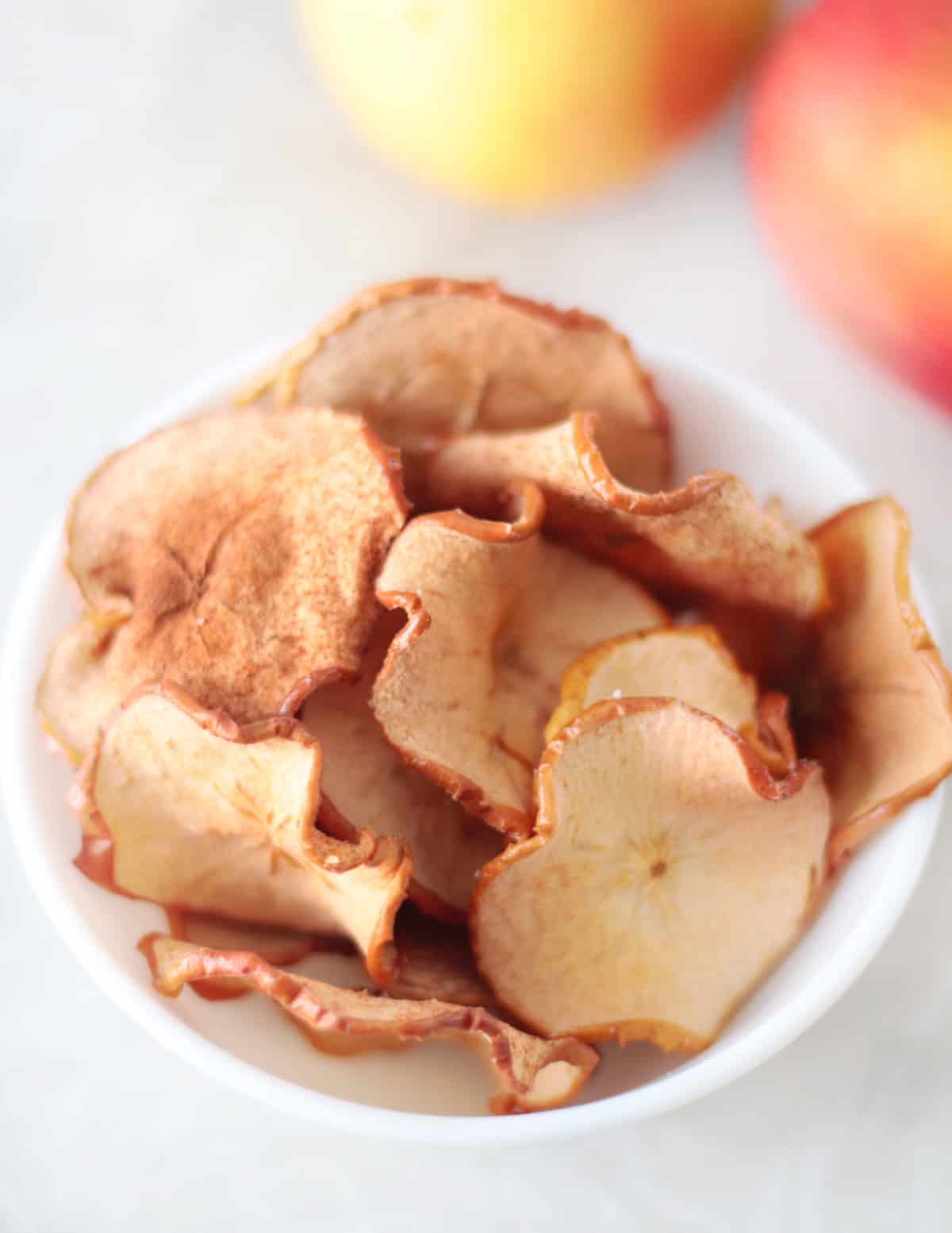 Small white bowl full of baked apple chips.