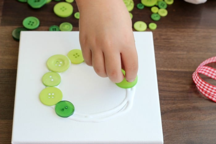 child gluing buttons onto canvas
