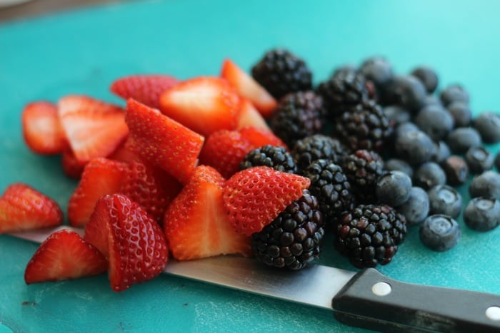 sliced strawberries blackberries and blueberries on cutting board