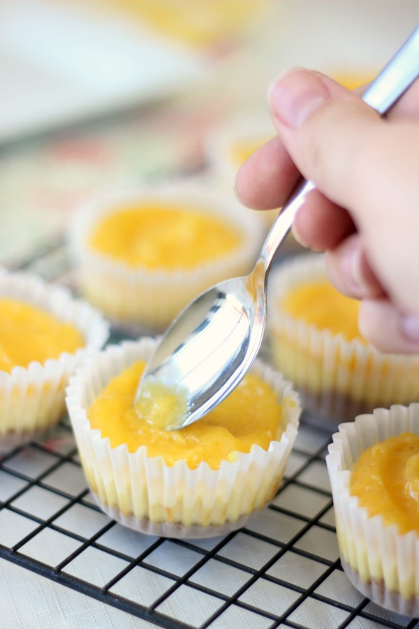 spoon spreading lemon curd on cheesecakes