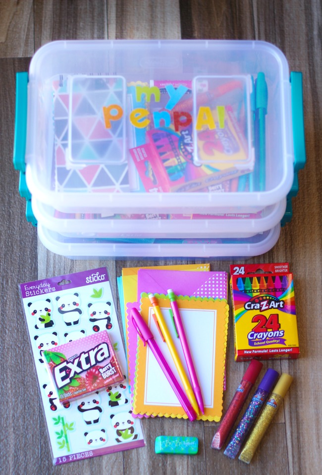 3 pen pal totes stacked on top of each other with assortment of stationary supplies next to them.