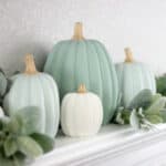 Painted pumpkins on a mantel with greenery.
