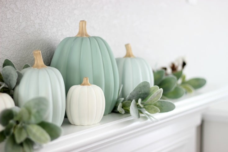 fireplace mantel with painted green pumpkins with greenery tucked in