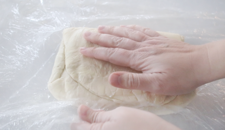 hand wrapping dough in palastic wrap