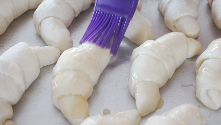 purple pastry brush brushing egg wash over unbaked croissants