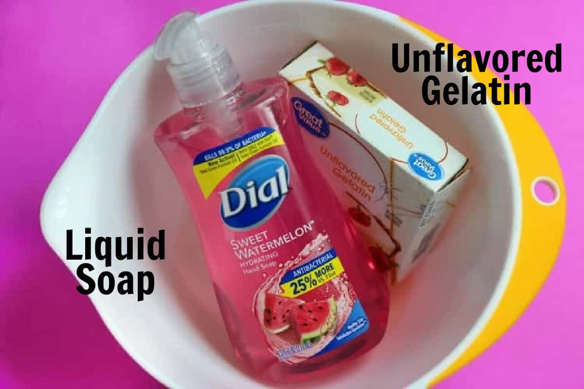 White bowl with a bottle of pink liquid soap and box of unflavored gelatin packets inside.
